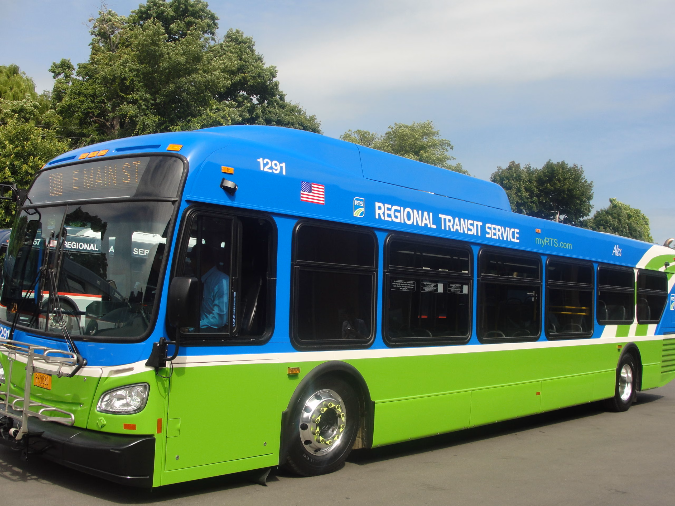 Blue and green RTS electric bus on city street.
