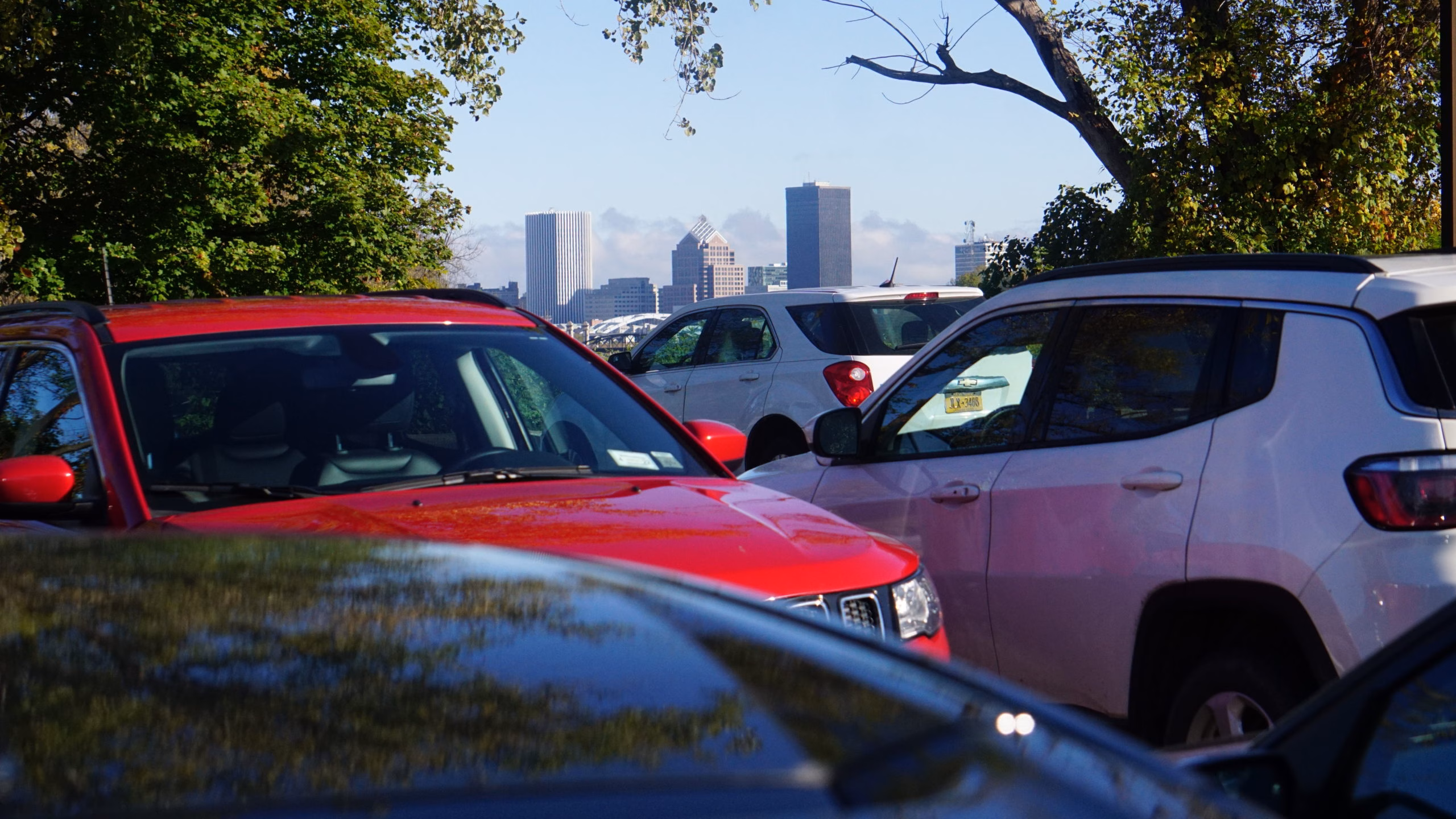 Red and white vehicles parked in lot with Rochester NY skyline in background.